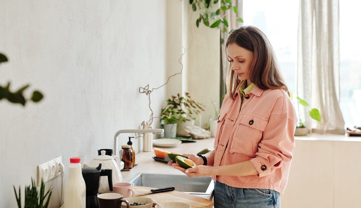 Woman preparing avocado in a modern kitchen with natural light.