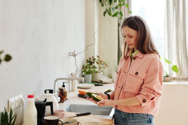 Woman preparing avocado in a modern kitchen with natural light.